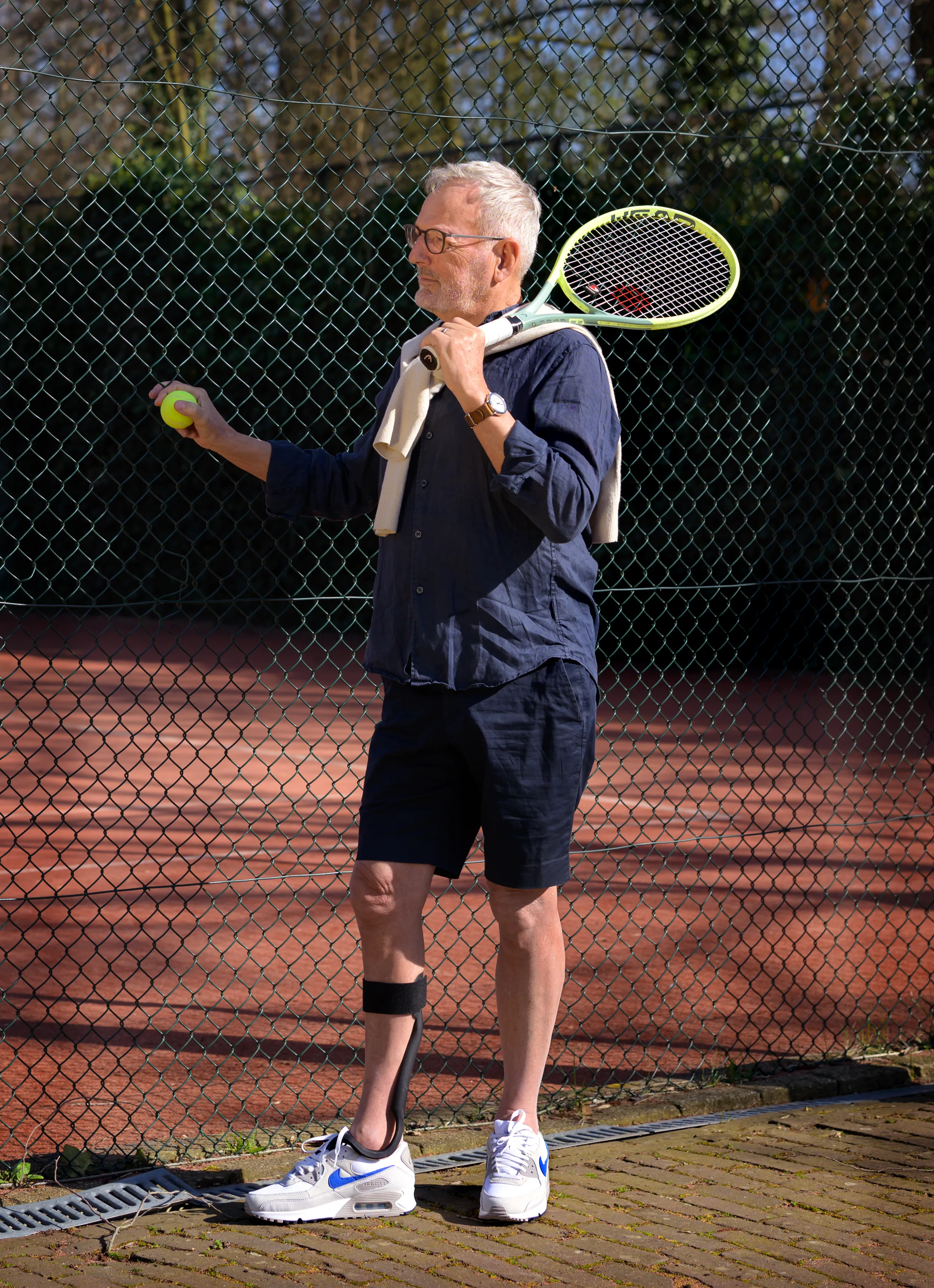 Een man op een tennisbaan met de Rise, racket over de schouder